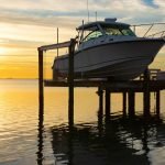 Expensive fishing boat on electric motorized dock vessel lift during sunrise with colorful sky.