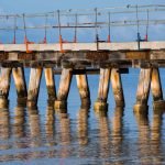 Old wooden pier under repair with timber pylons reflected in the water.